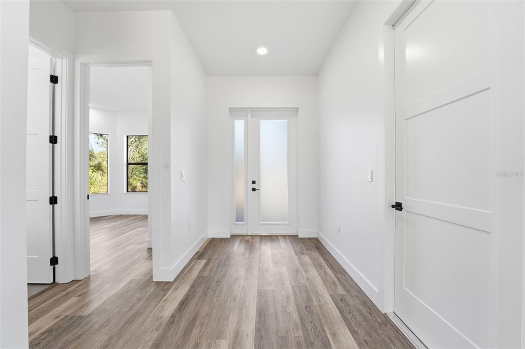 A bright entryway features white walls, light wood-look flooring, and a modern glass-paneled front door — 12005 CARNIVAL AVENUE, PORT CHARLOTTE, FL