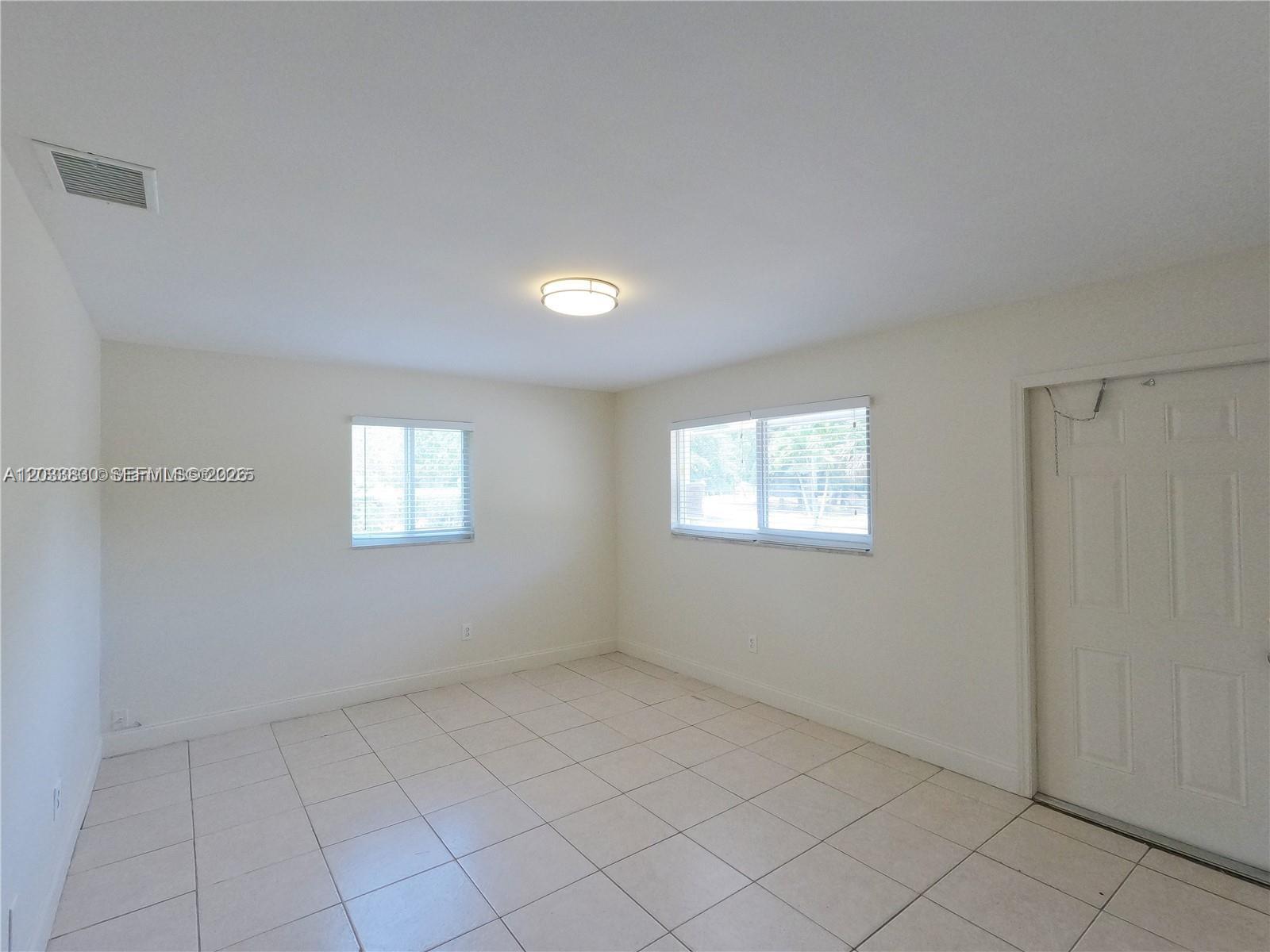 An empty room features white walls, tiled flooring, two windows, and a white door — 4938 Serafica Dr # 14, Lake Worth FL 33461, LAKE WORTH, FL