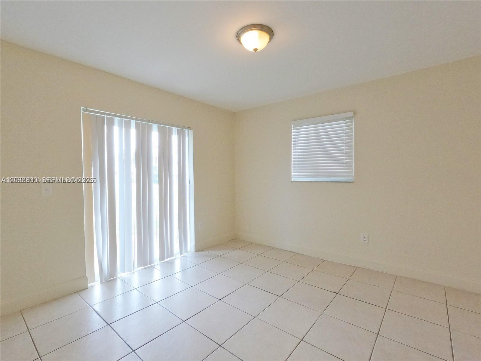 An empty room features beige walls, light-colored tile flooring, a ceiling light, and vertical blinds — 4938 Serafica Dr # 14, Lake Worth FL 33461, LAKE WORTH, FL
