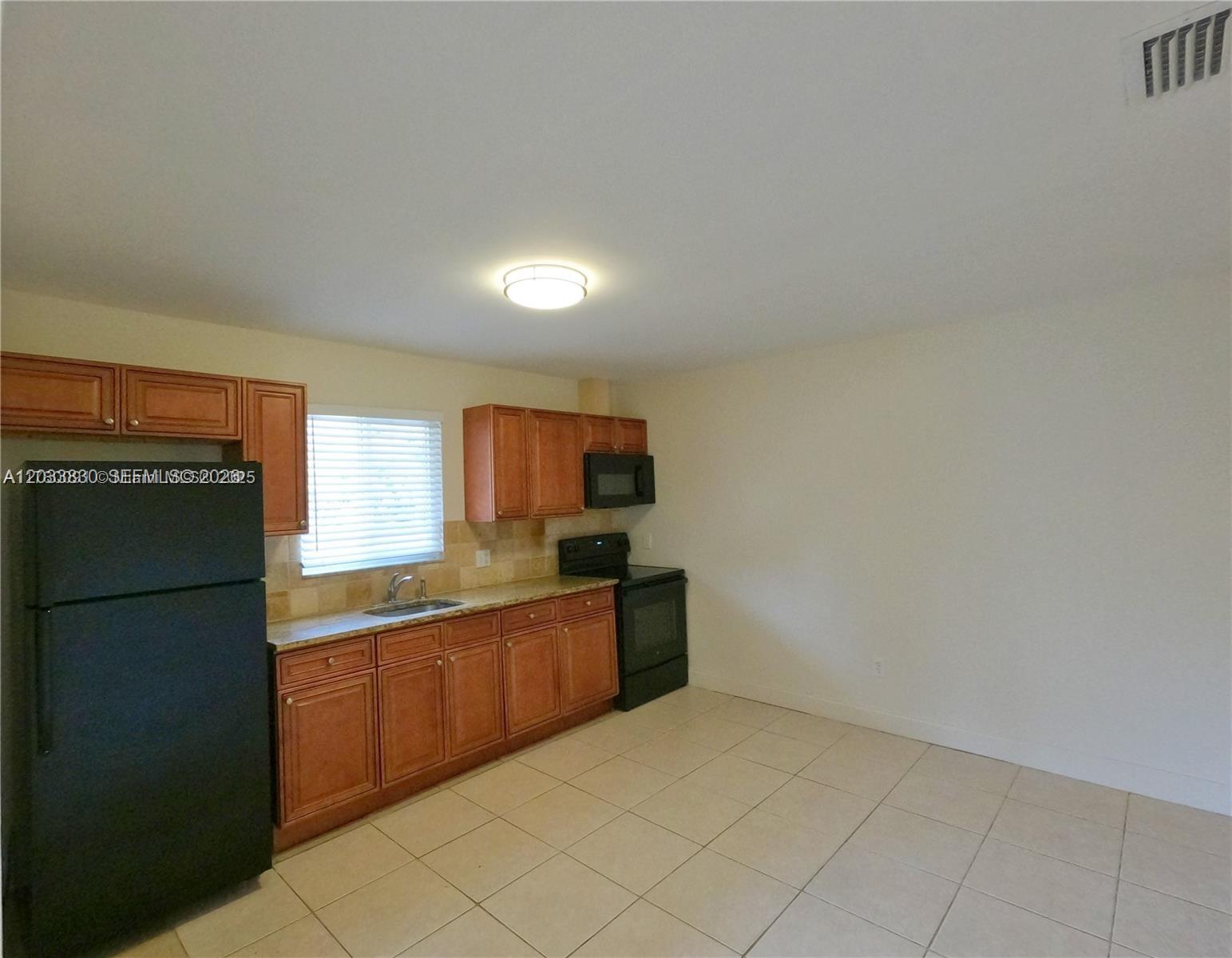 A kitchen features wooden cabinets, black appliances, a window, and light-colored tile flooring — 4938 Serafica Dr # 14, Lake Worth FL 33461, LAKE WORTH, FL