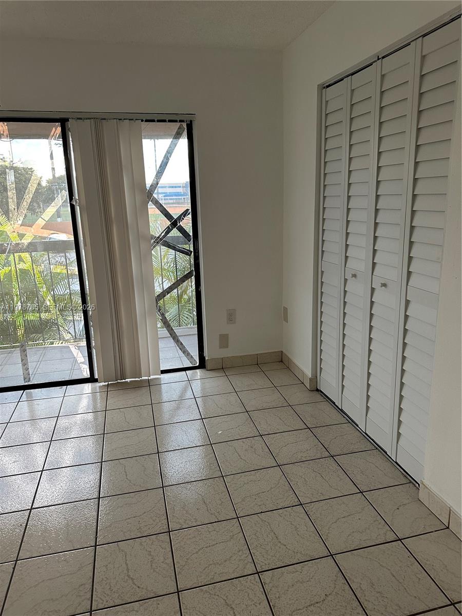 A room with white walls, tiled floors, a sliding glass door, and white louvered closet doors — 2194 W 60th St # 22213, Hialeah FL 33016, HIALEAH, FL