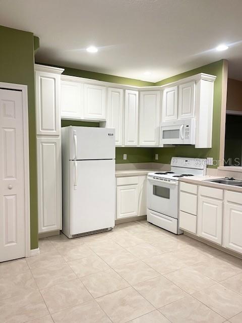 A kitchen features white cabinets, white appliances, and light-colored tile flooring against olive green walls — 6012 PARKSIDE MEADOW DRIVE, TAMPA, FL