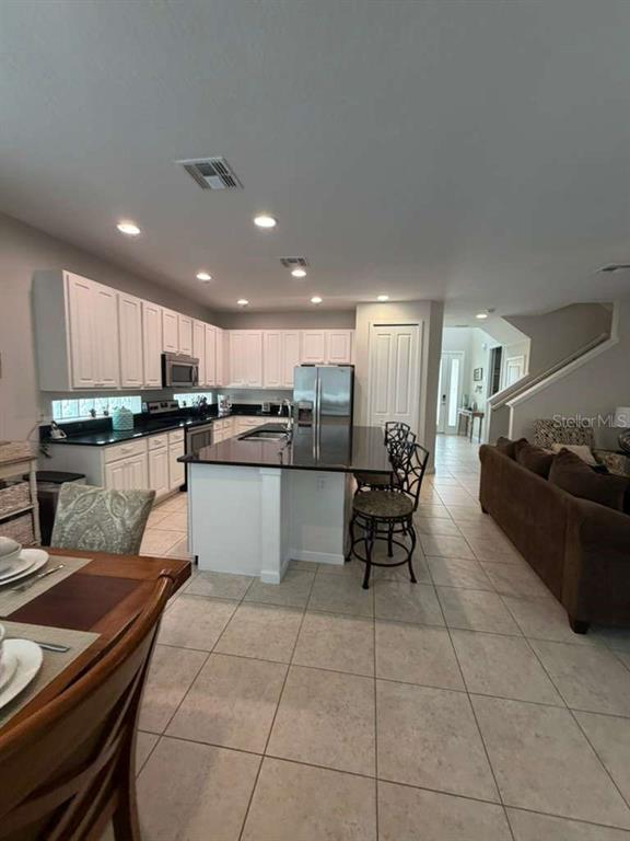 A kitchen with white cabinets and a dark island opens into a living area — 4507 MONADO DRIVE, KISSIMMEE, FL