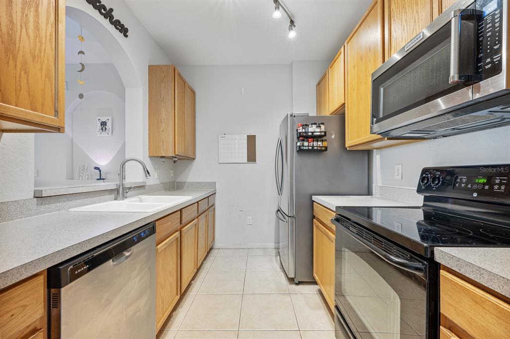 A galley kitchen features light wood cabinets, stainless steel appliances, and light-colored tile flooring — 6335 CONTESSA DRIVE UNIT 301, ORLANDO, FL