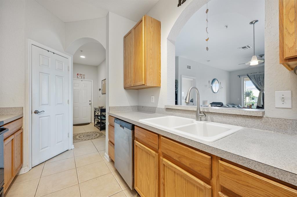 A kitchen features oak cabinets, a white double-basin sink, and a view into the living area — 6335 CONTESSA DRIVE UNIT 301, ORLANDO, FL