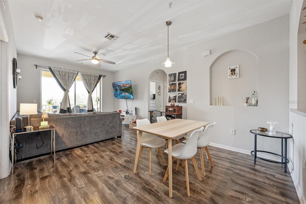 An open-concept living and dining area features wood-look flooring, a gray sectional, and white chairs — 6335 CONTESSA DRIVE UNIT 301, ORLANDO, FL