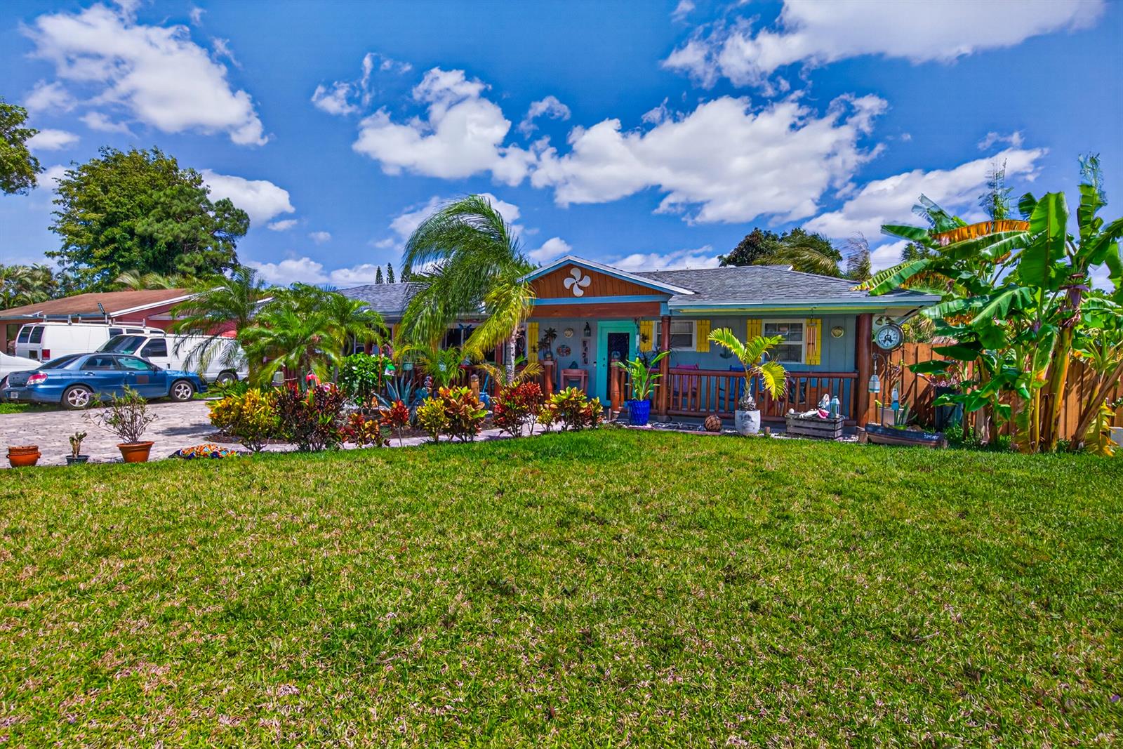 A single-story house with a blue exterior, wooden porch, and tropical landscaping under a blue sky — 5135 Palm Ridge Boulevard, Delray Beach FL 33484, DELRAY BEACH, FL