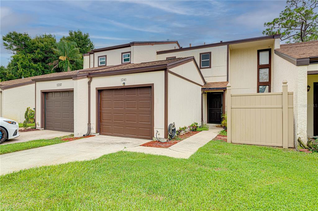 The exterior of a two-story townhouse features two garage doors, a tan fence, and grass — 1241 SAINT ANDREWS DRIVE, ROCKLEDGE, FL