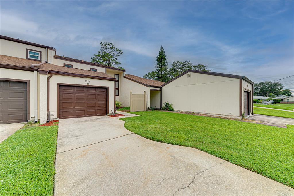 A beige townhouse exterior features a brown garage door, a concrete driveway, and a grassy lawn — 1241 SAINT ANDREWS DRIVE, ROCKLEDGE, FL