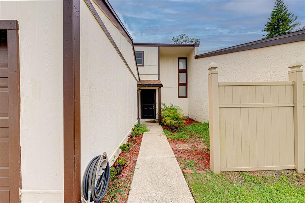 A concrete walkway leads to the front entrance of a house with beige stucco walls — 1241 SAINT ANDREWS DRIVE, ROCKLEDGE, FL