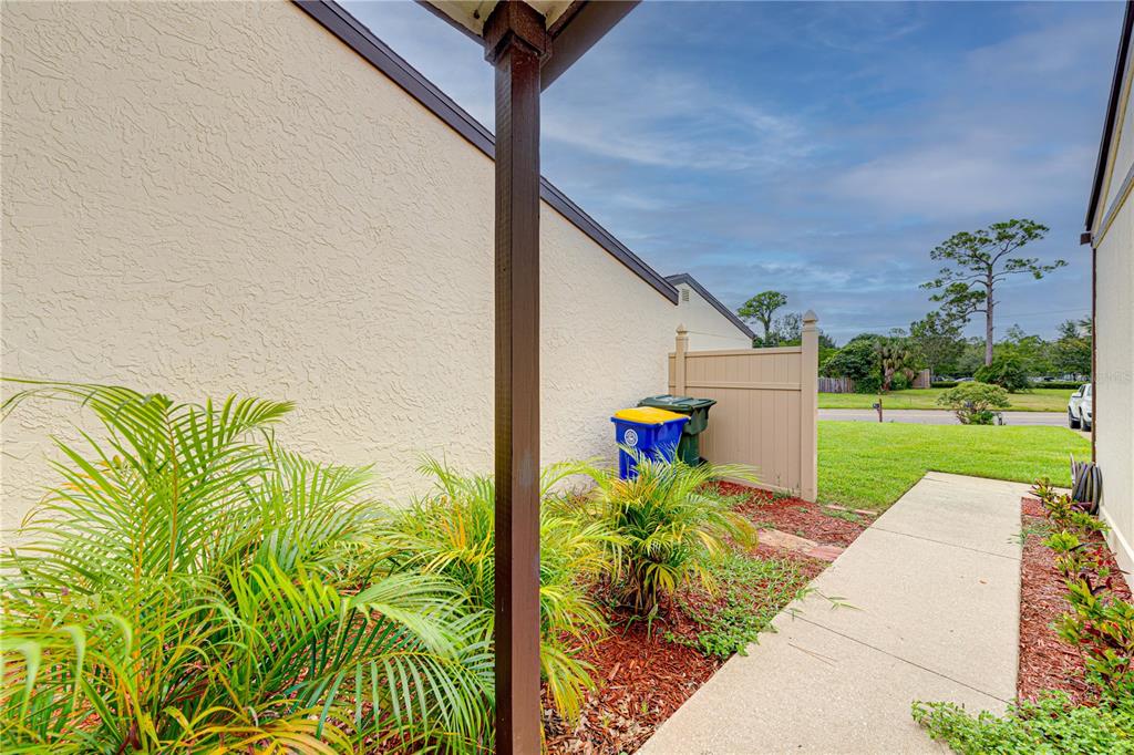 A concrete walkway leads past a small palm garden and trash bins toward a grassy lawn — 1241 SAINT ANDREWS DRIVE, ROCKLEDGE, FL