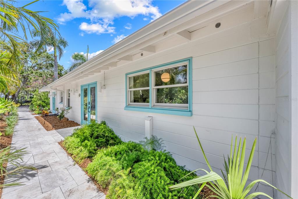 A white house exterior features turquoise window and door frames along a stone walkway — 3360 HIGEL AVENUE, SARASOTA, FL