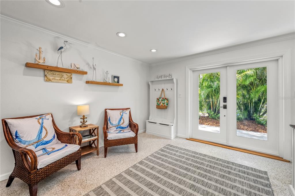 A coastal-themed entryway features two wicker chairs, a white storage bench, and glass double doors — 3360 HIGEL AVENUE, SARASOTA, FL