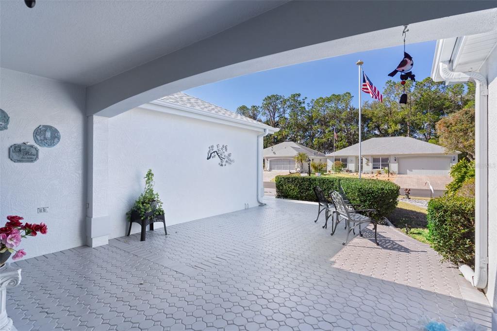 A covered patio features light-colored patterned pavers, a white wall, and outdoor seating — 1115 SALIDO AVENUE, THE VILLAGES, FL