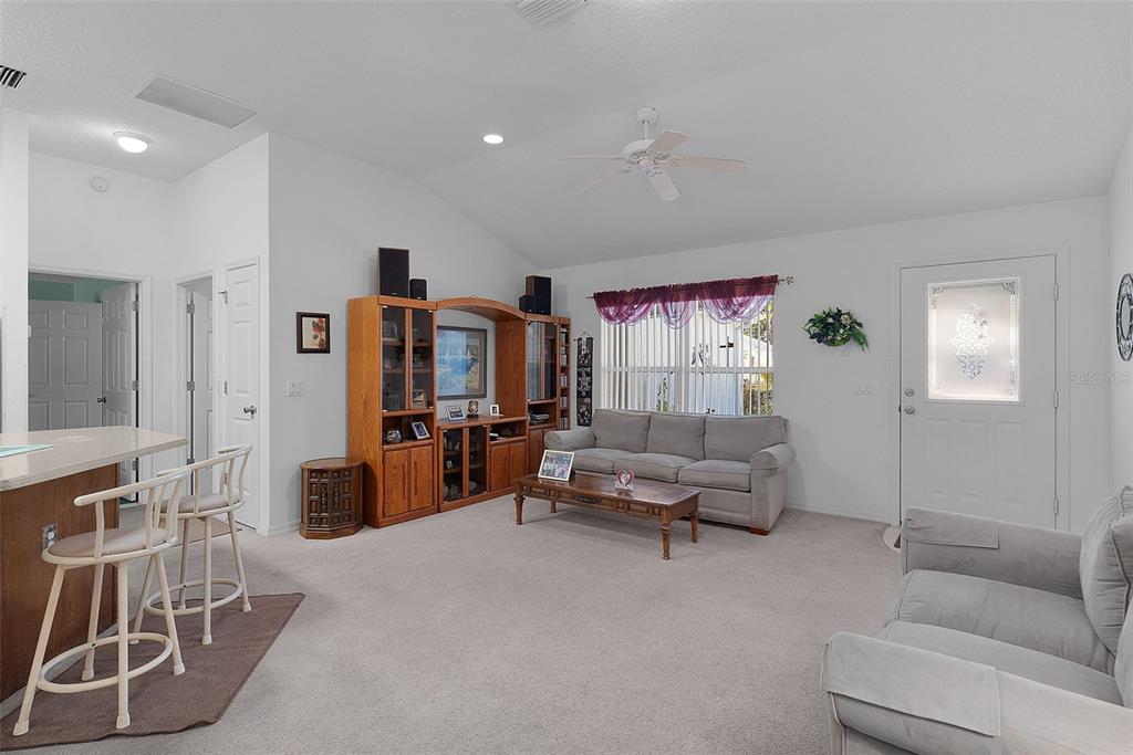 A living room features a vaulted ceiling, carpeted floors, a wooden entertainment center, and seating — 1115 SALIDO AVENUE, THE VILLAGES, FL