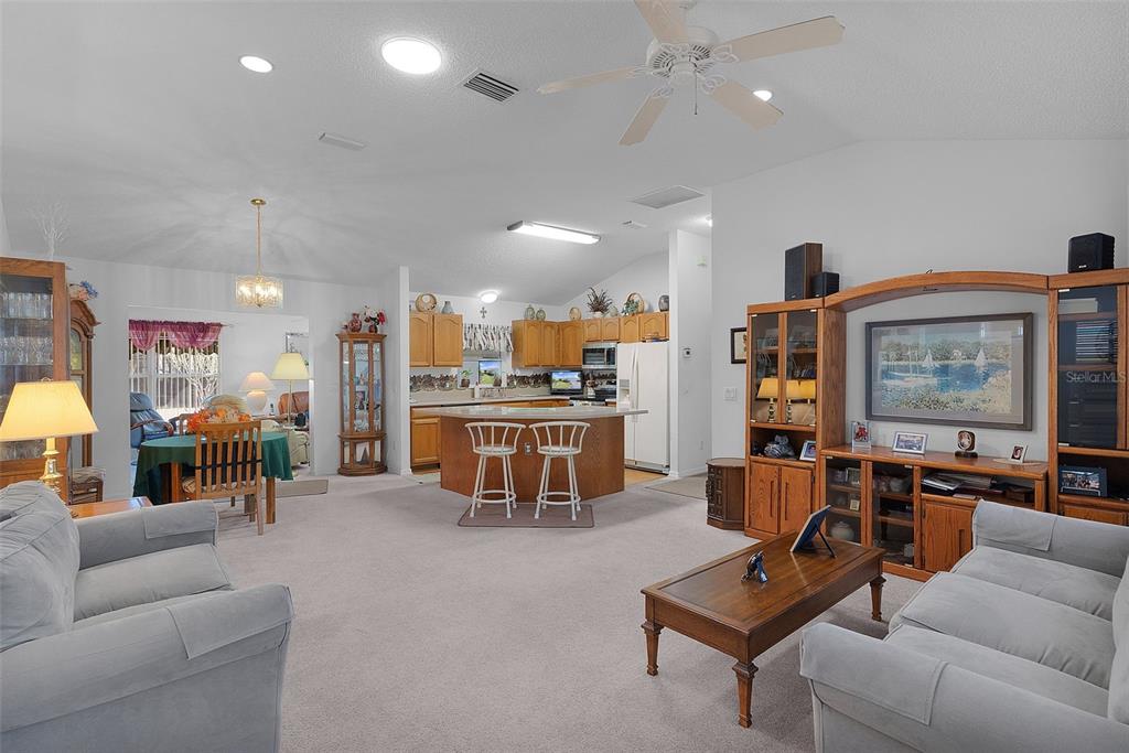 A living room with light carpet opens to a kitchen with wood cabinets and island — 1115 SALIDO AVENUE, THE VILLAGES, FL