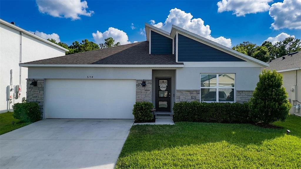 A single-story house features a two-car garage, stone accents, and blue siding under a sky — 5154 TANA TERRACE, ST CLOUD, FL
