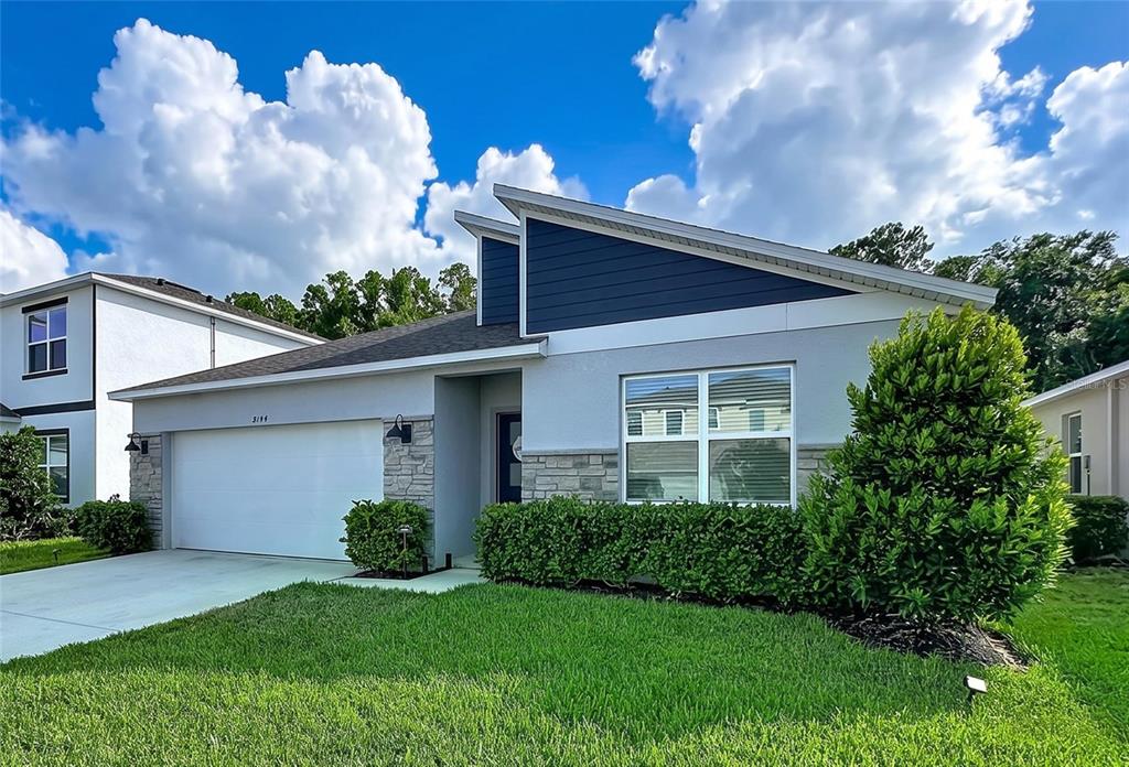 A modern single-story house features a shed roof, gray stucco, stone accents, and a two-car garage — 5154 TANA TERRACE, ST CLOUD, FL