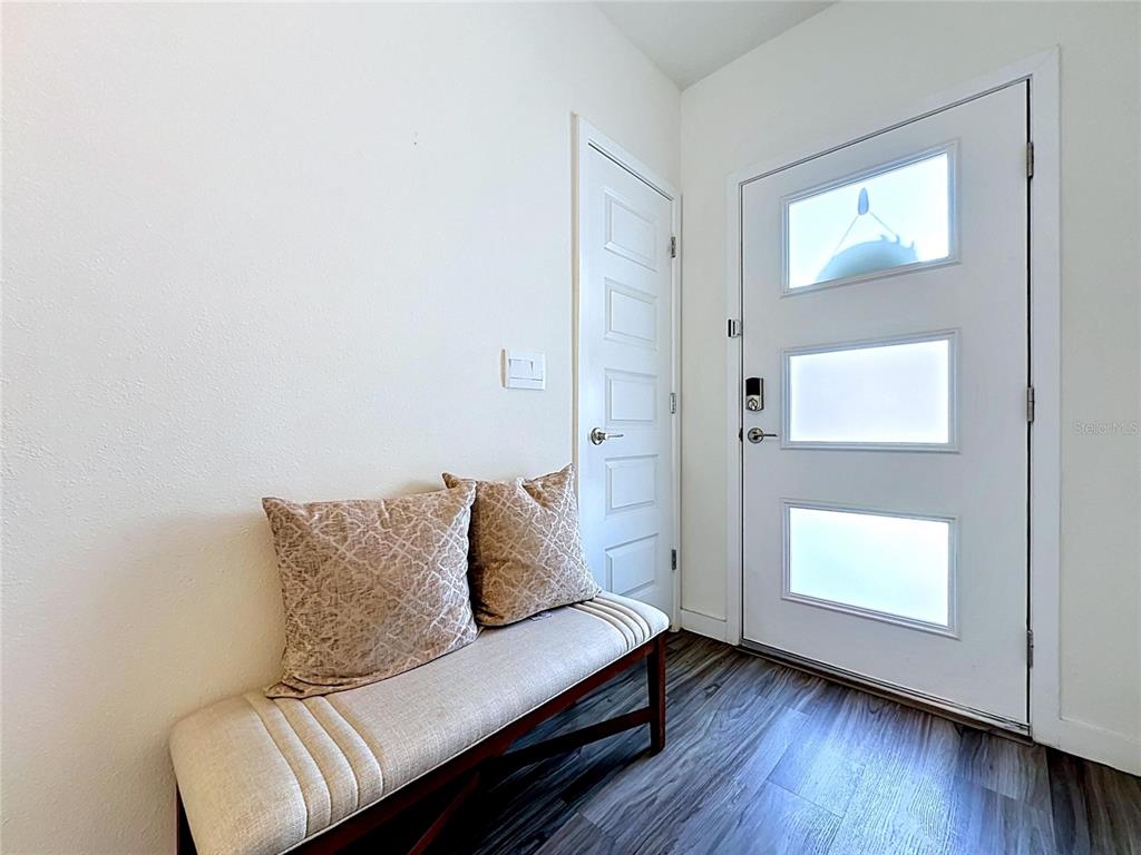 An entryway features a bench with two pillows, a white door, and wood-look flooring — 5154 TANA TERRACE, ST CLOUD, FL