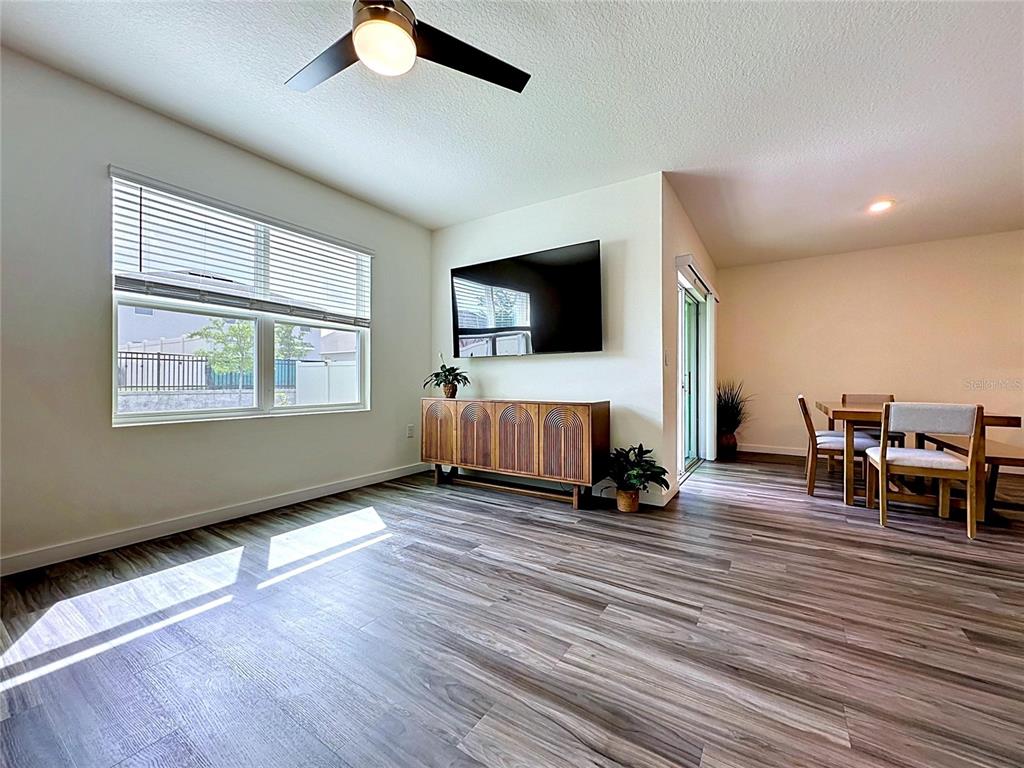 A living room features wood-look flooring, a wall-mounted television, and an adjacent dining area — 5154 TANA TERRACE, ST CLOUD, FL