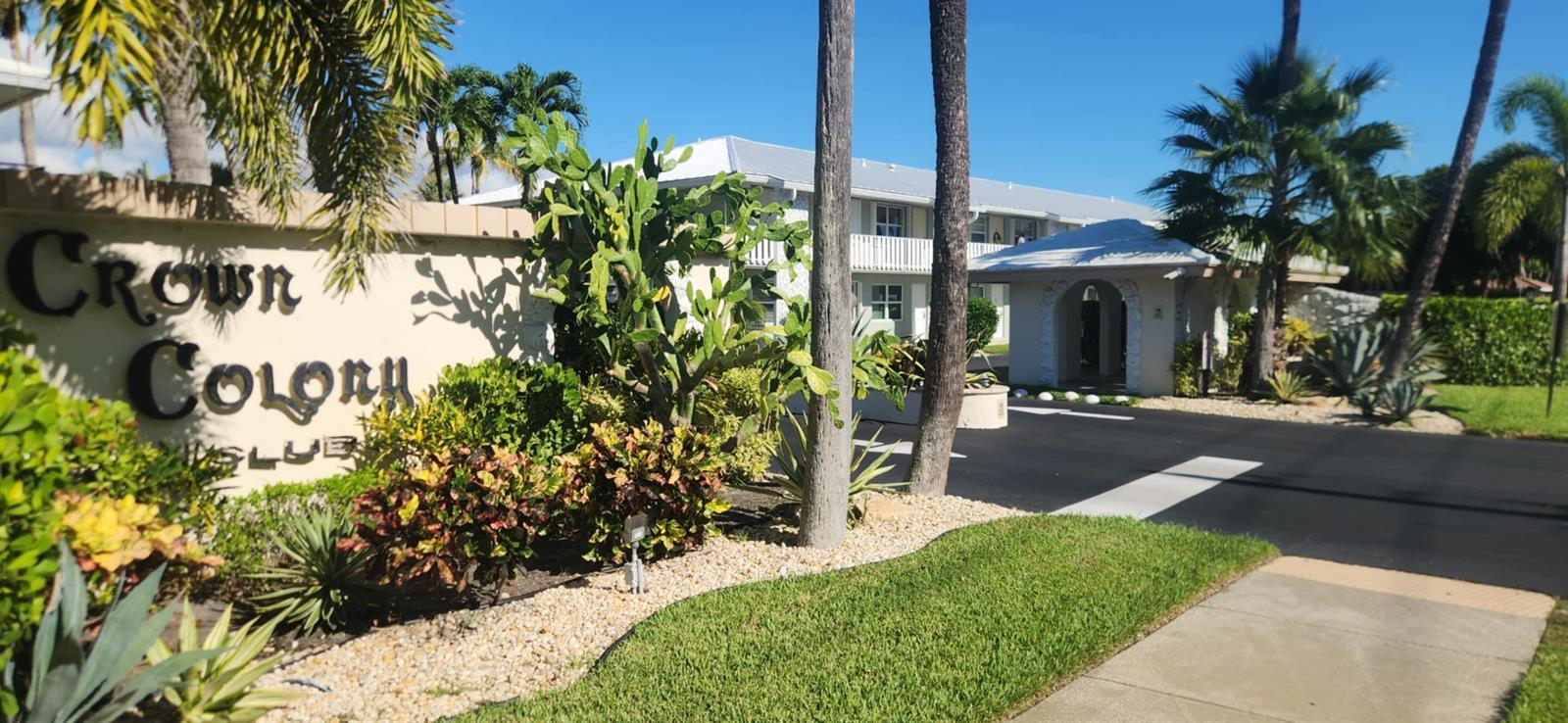 The entrance to the Crown Colony Club features a sign, palm trees, and landscaping — 5550 N Ocean Boulevard # 106, Ocean Ridge FL 33435, OCEAN RIDGE, FL