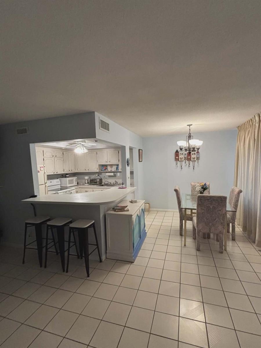 A kitchen with white cabinets and a breakfast bar overlooks a dining area with tile — 5550 N Ocean Boulevard # 106, Ocean Ridge FL 33435, OCEAN RIDGE, FL