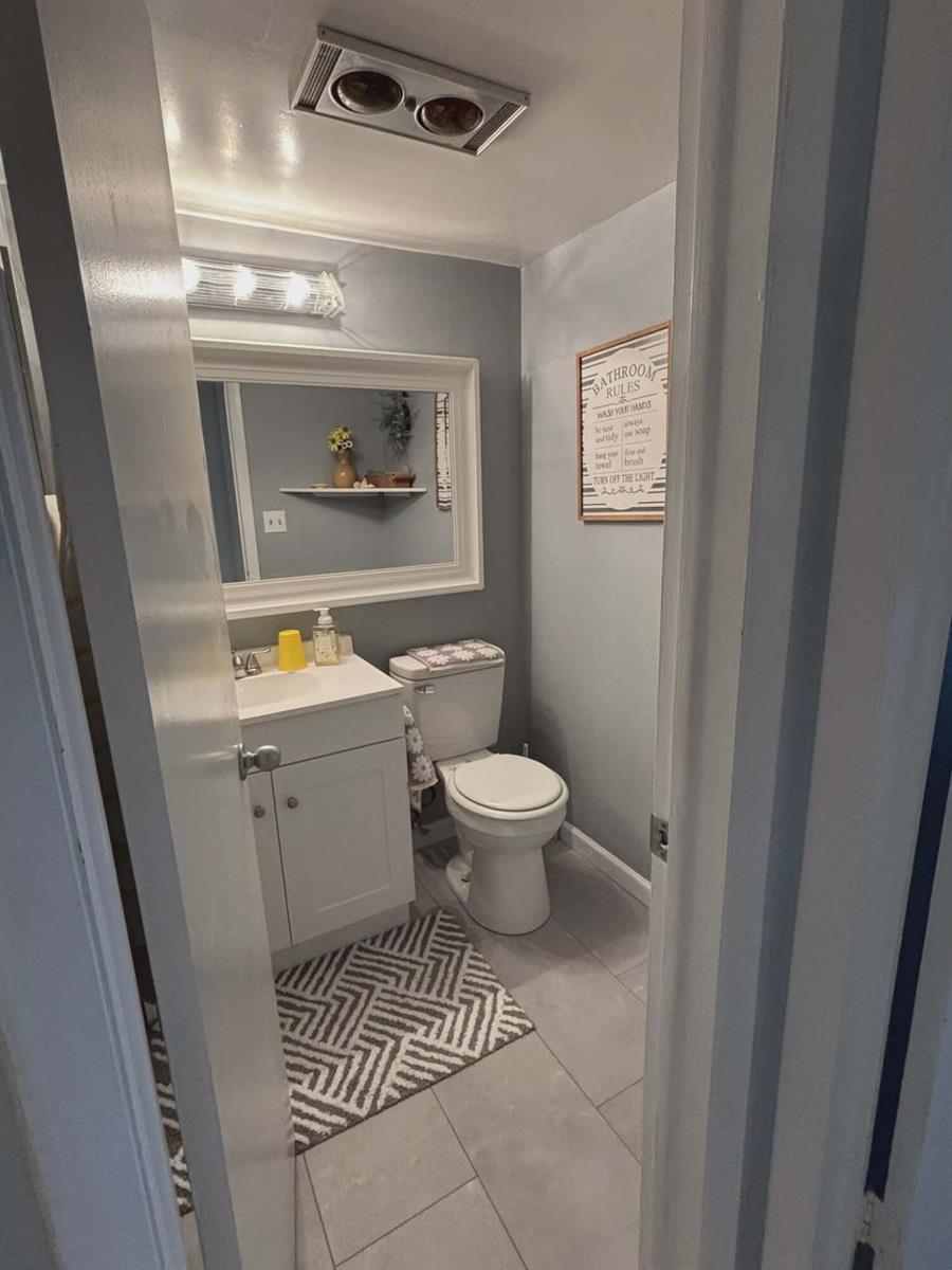 A small bathroom features a white vanity, a toilet, a mirror, and gray tiled flooring — 5550 N Ocean Boulevard # 106, Ocean Ridge FL 33435, OCEAN RIDGE, FL