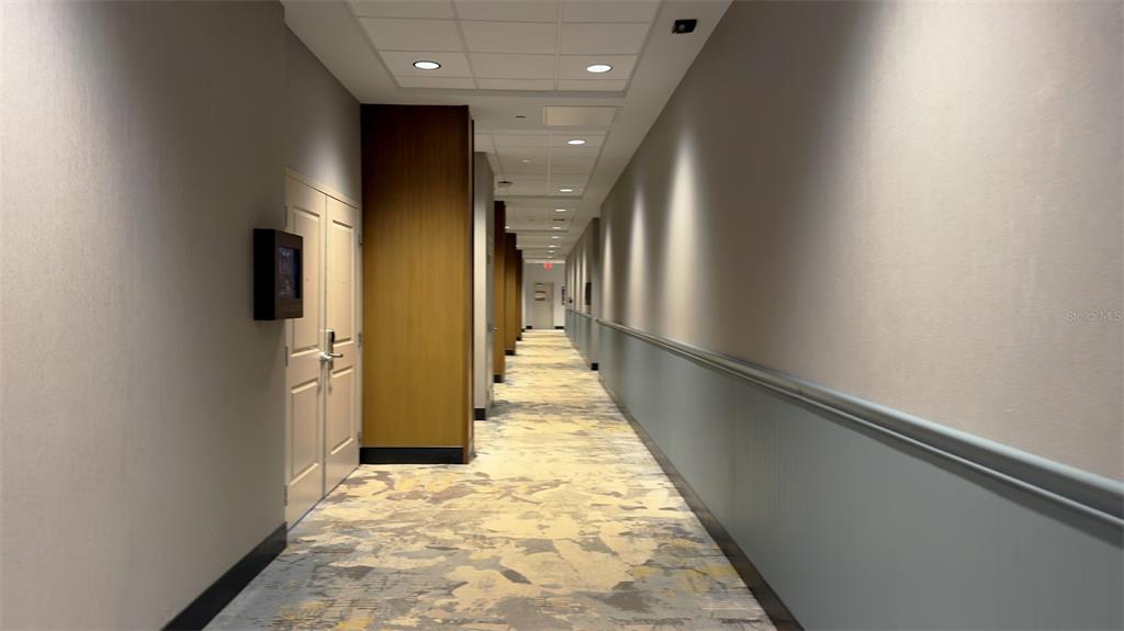 A long hotel hallway features patterned carpeting, light-colored walls, and a series of doors — 14501 GROVE RESORT AVENUE UNIT 3211, WINTER GARDEN, FL