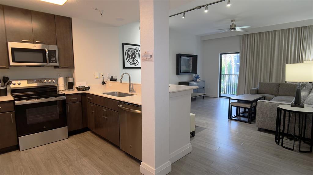 A kitchen with dark wood cabinets and stainless steel appliances opens into a living area — 14501 GROVE RESORT AVENUE UNIT 3211, WINTER GARDEN, FL