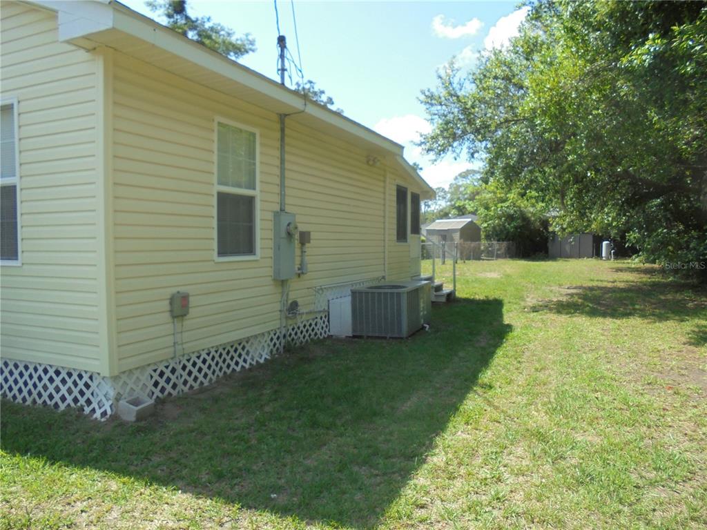 The exterior side of a yellow house features a central air conditioning unit and lattice skirting — 1510 NE 55TH STREET, OCALA, FL