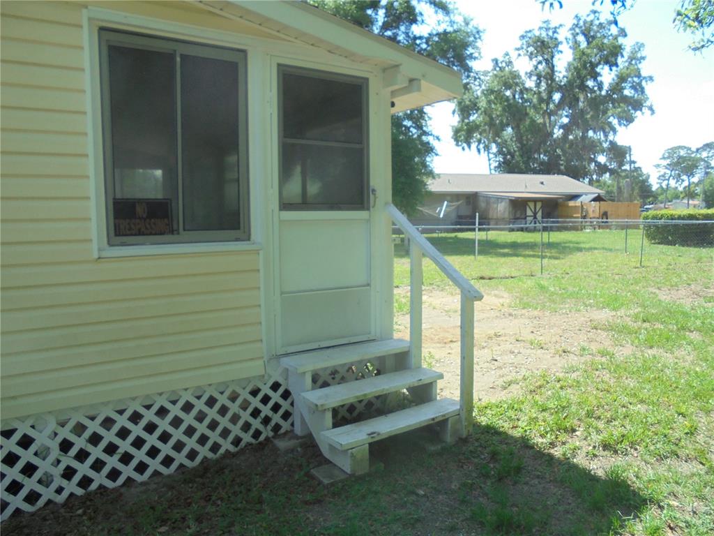 A white exterior door with a screen leads to wooden steps beside a yellow house — 1510 NE 55TH STREET, OCALA, FL