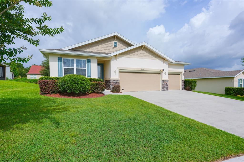 A single-story house with a beige exterior, stone accents, and a three-car garage — 2544 AUTUMN STREAM DRIVE, LEESBURG, FL