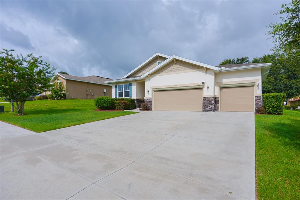 A single-story house with a three-car garage, stone accents, and a concrete driveway — 2544 AUTUMN STREAM DRIVE, LEESBURG, FL