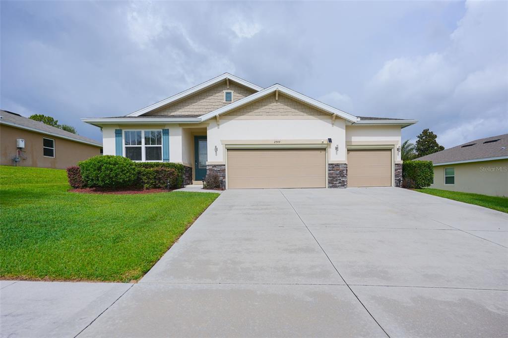 A single-story house with a beige stucco exterior, stone accents, and a three-car garage — 2544 AUTUMN STREAM DRIVE, LEESBURG, FL