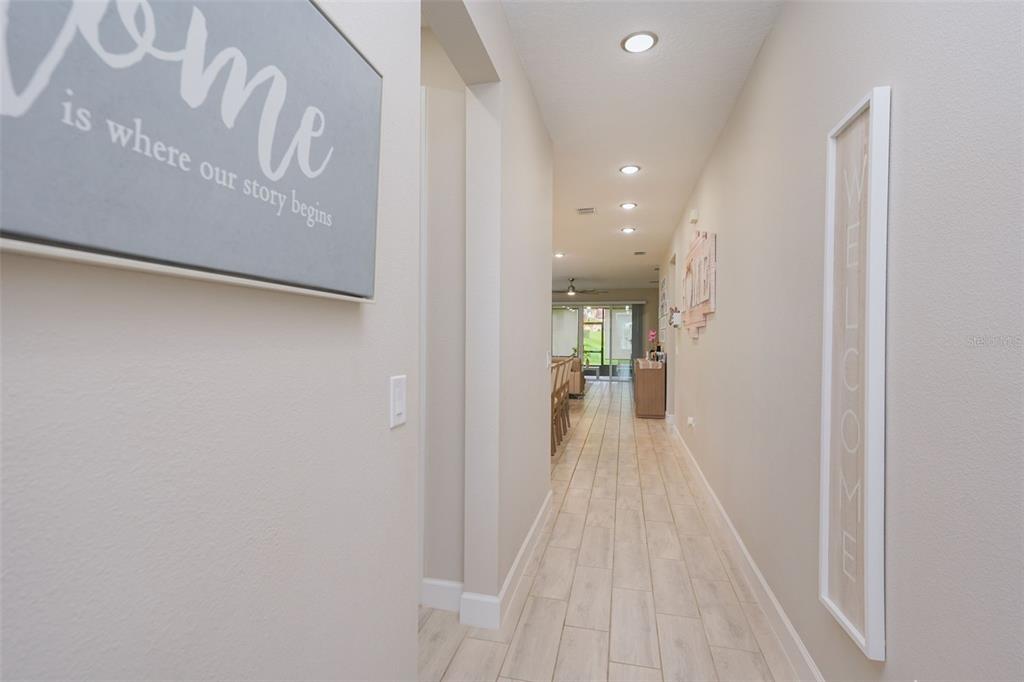 A long, narrow hallway with light-colored tile flooring leads to an open living area — 2544 AUTUMN STREAM DRIVE, LEESBURG, FL