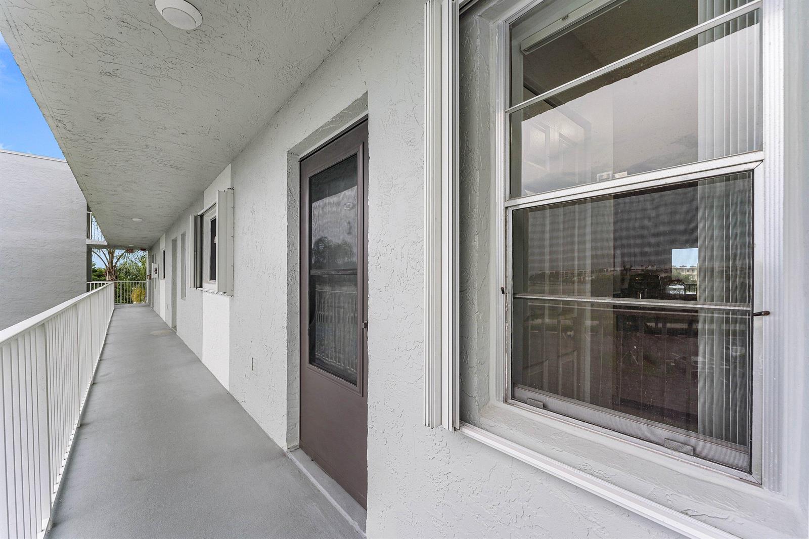 An exterior view of a concrete apartment building walkway with a door and windows — 2222 N Cypress Bend Drive # 403, Pompano Beach FL 33069, POMPANO BEACH, FL