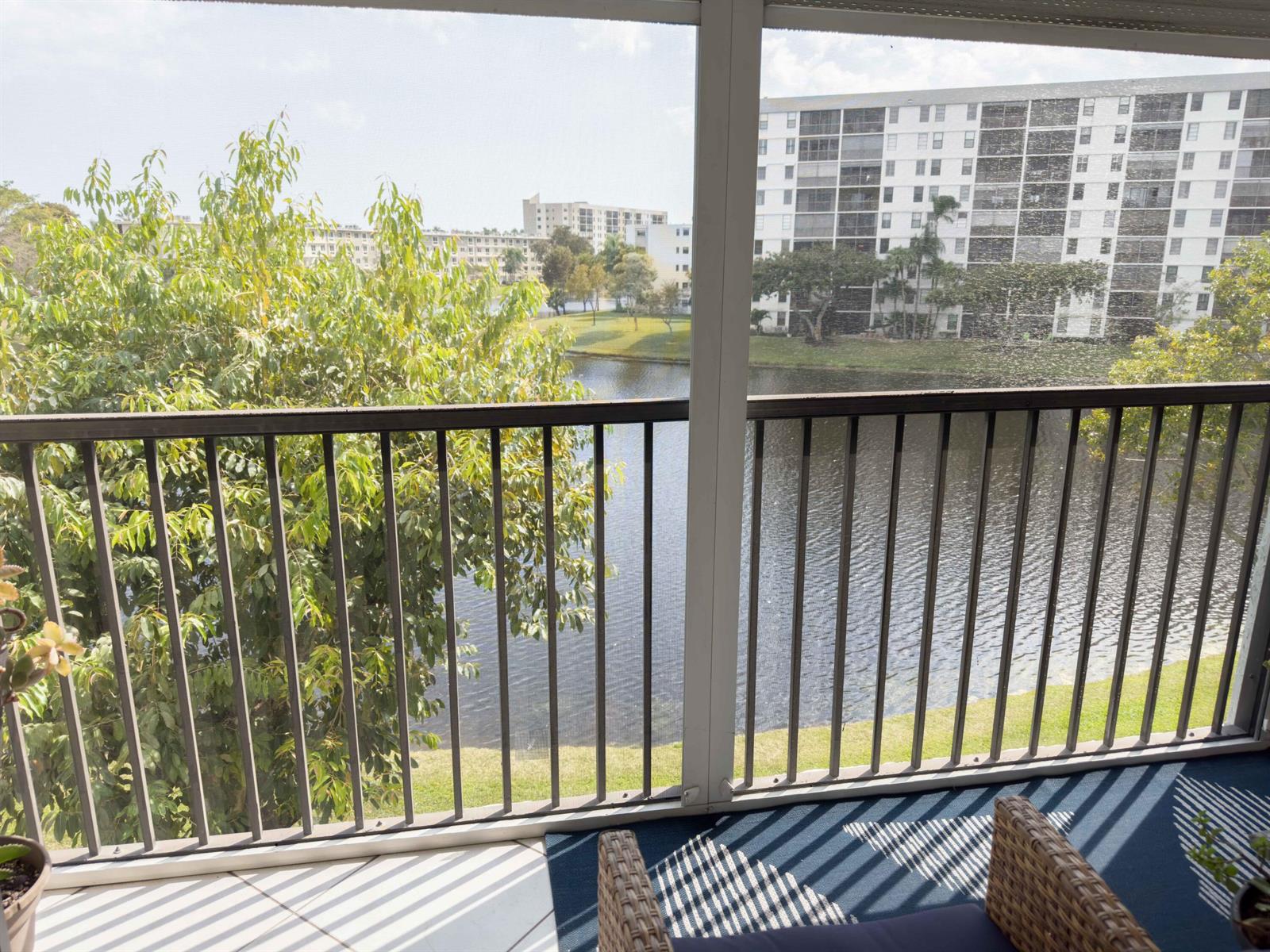 A screened-in balcony overlooks a lake and a multi-story apartment building — 2222 N Cypress Bend Drive # 403, Pompano Beach FL 33069, POMPANO BEACH, FL