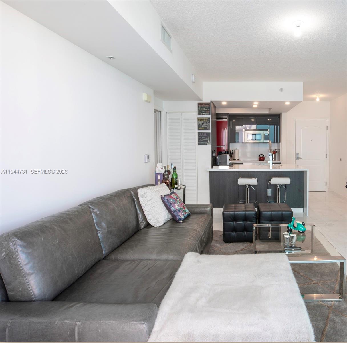 A living room with a grey leather sofa opens into a kitchen with bar seating — 110 Washington Ave # 1722, Miami Beach FL 33139, MIAMI BEACH, FL