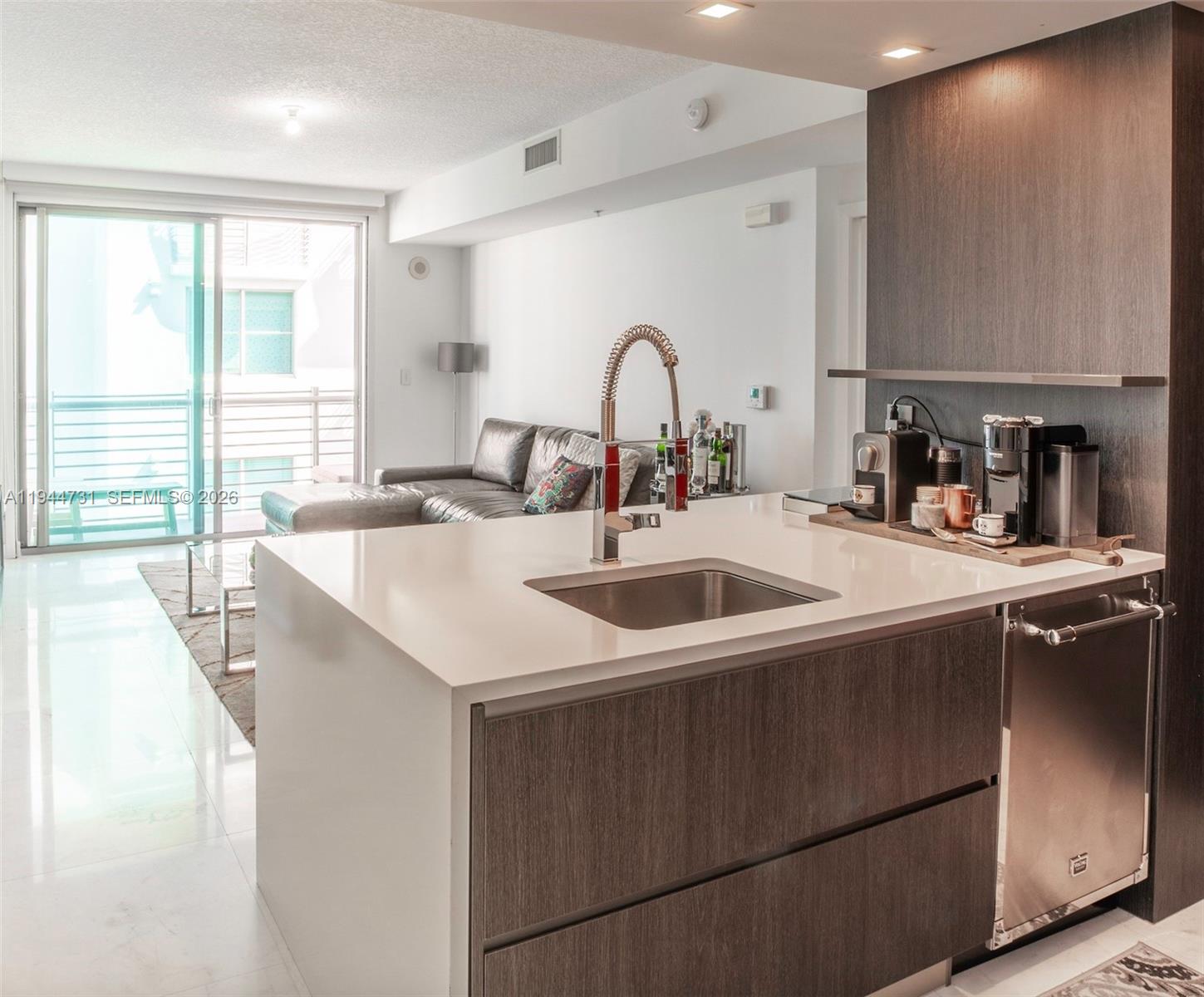 A modern kitchen island with a sink and dark wood cabinetry faces a living area — 110 Washington Ave # 1722, Miami Beach FL 33139, MIAMI BEACH, FL