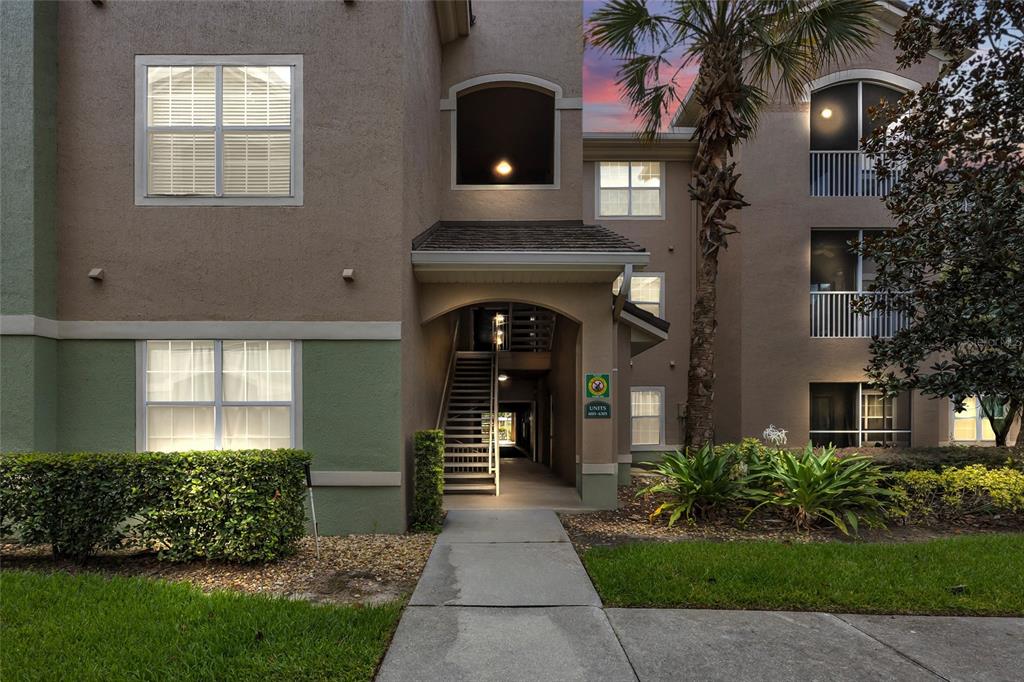 An exterior view of a multi-story apartment building with a central staircase and landscaping — 4897 CYPRESS WOODS DRIVE UNIT 6303, ORLANDO, FL