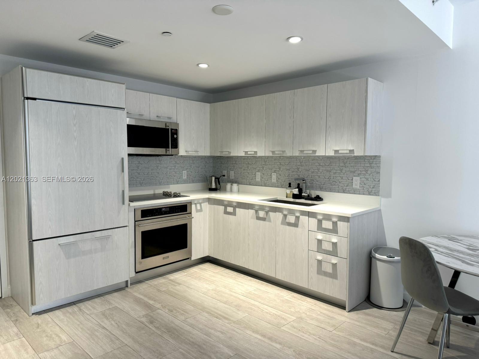 A modern kitchen features light wood-grain cabinetry, stainless steel appliances, and a gray tiled backsplash — 45 SW 9th St # 3107, Miami FL 33130, MIAMI, FL