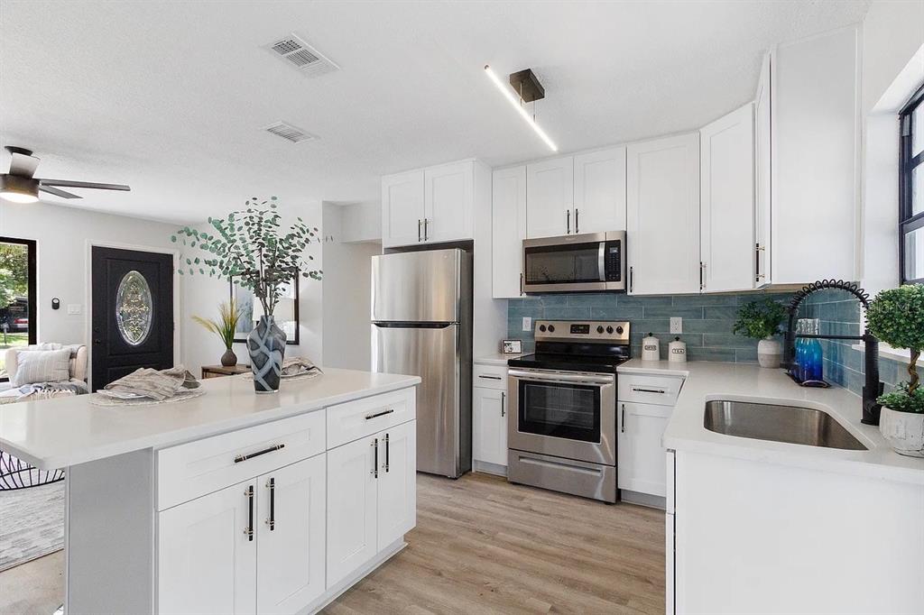 A modern kitchen features white cabinets, stainless steel appliances, and a blue tiled backsplash — 4721 W WISCONSIN AVENUE, TAMPA, FL