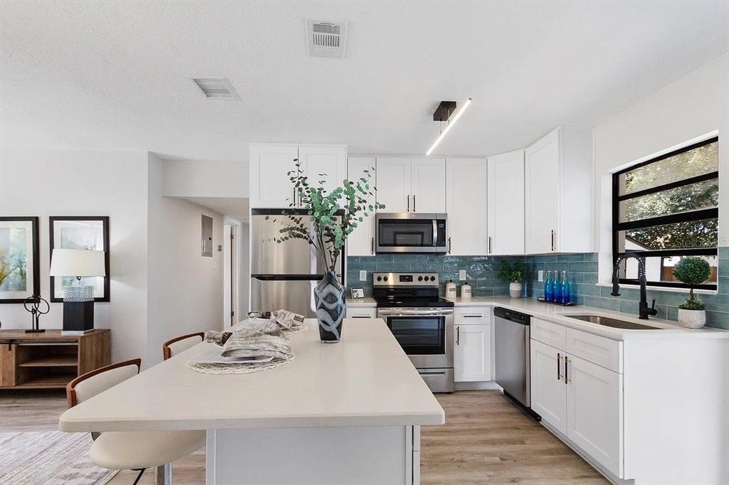 A modern kitchen features white cabinets, a central island, and a blue tiled backsplash — 4721 W WISCONSIN AVENUE, TAMPA, FL
