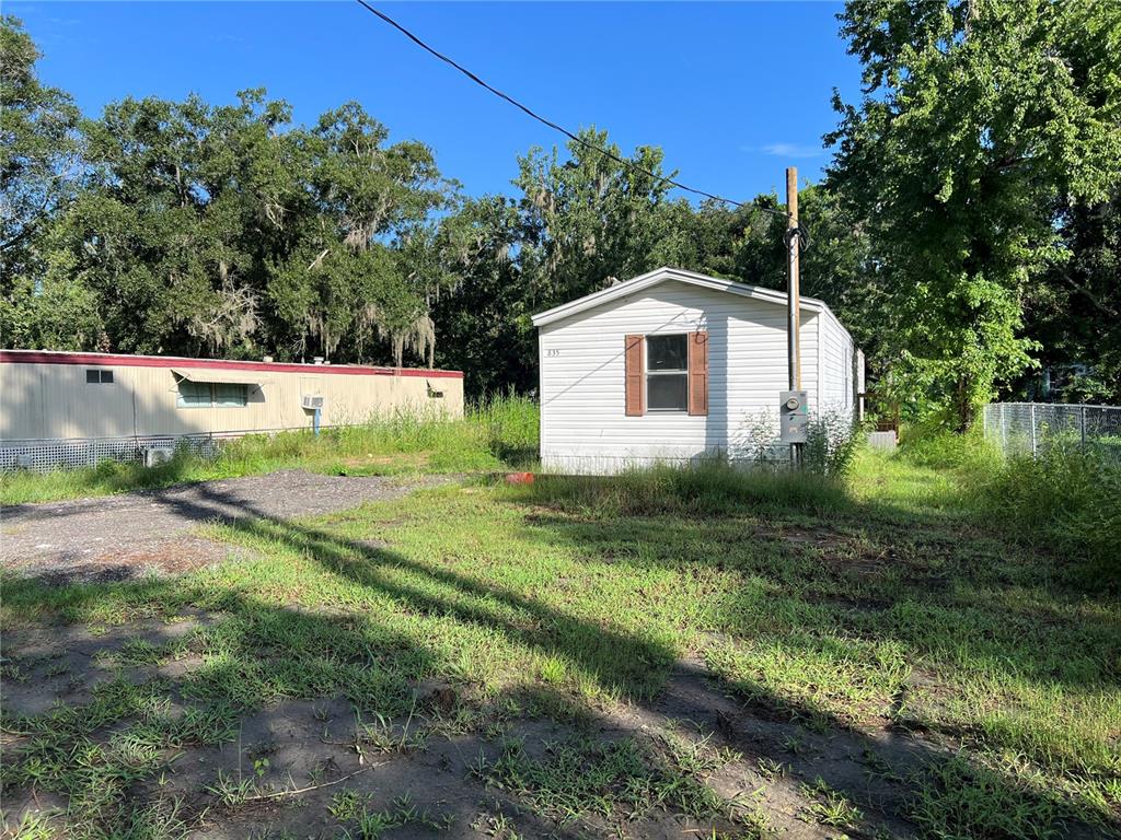 A white mobile home sits on a grassy lot next to a larger structure — 835 MEMPHIS ROAD, LAKELAND, FL