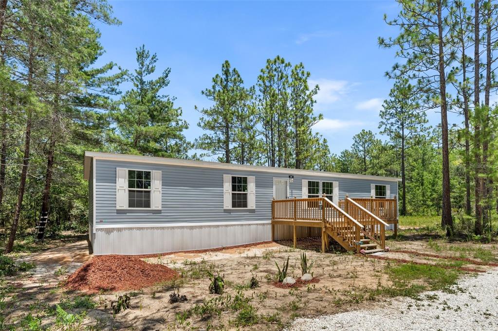 A light blue manufactured home with a wooden deck sits in a wooded lot — 419 LILY TRAIL, INTERLACHEN, FL