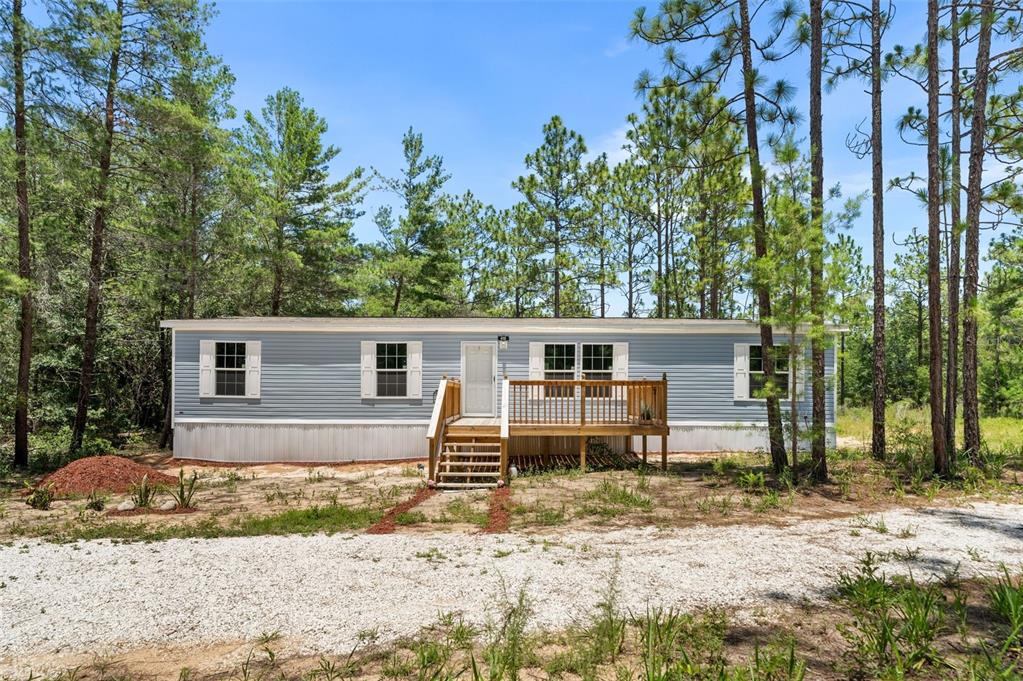 A light blue manufactured home sits in a wooded lot with a wooden front deck — 419 LILY TRAIL, INTERLACHEN, FL