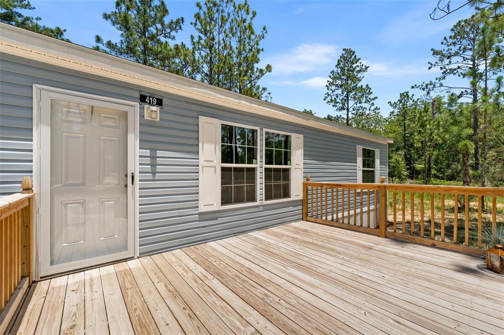 A wooden deck leads to the front door of a light blue mobile home — 419 LILY TRAIL, INTERLACHEN, FL