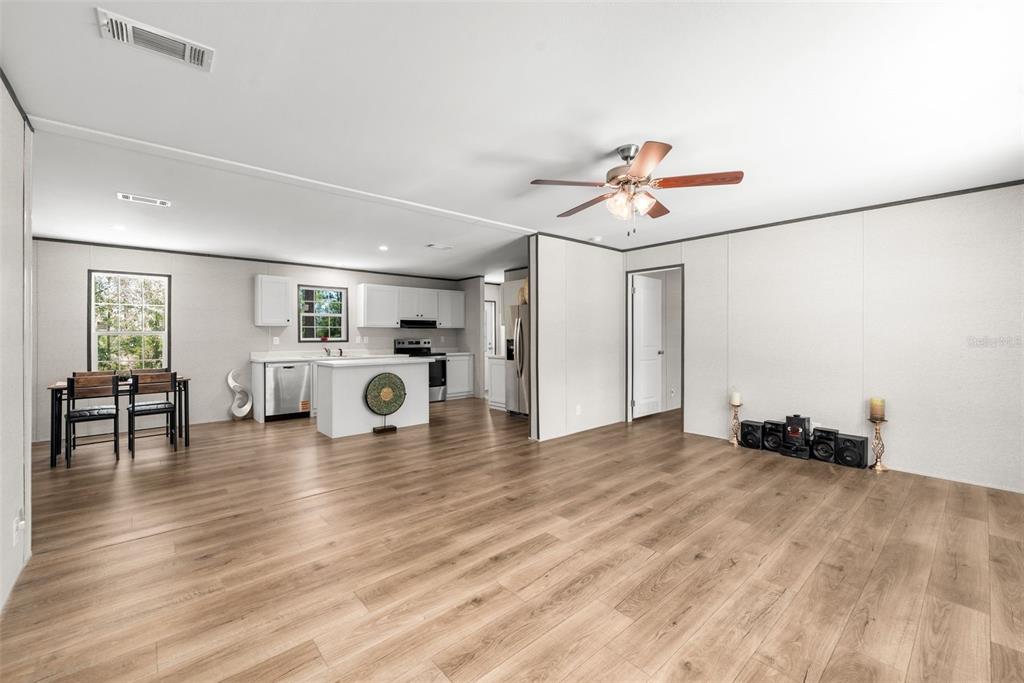 An open-concept living room and kitchen with light wood-look flooring and white cabinetry — 419 LILY TRAIL, INTERLACHEN, FL