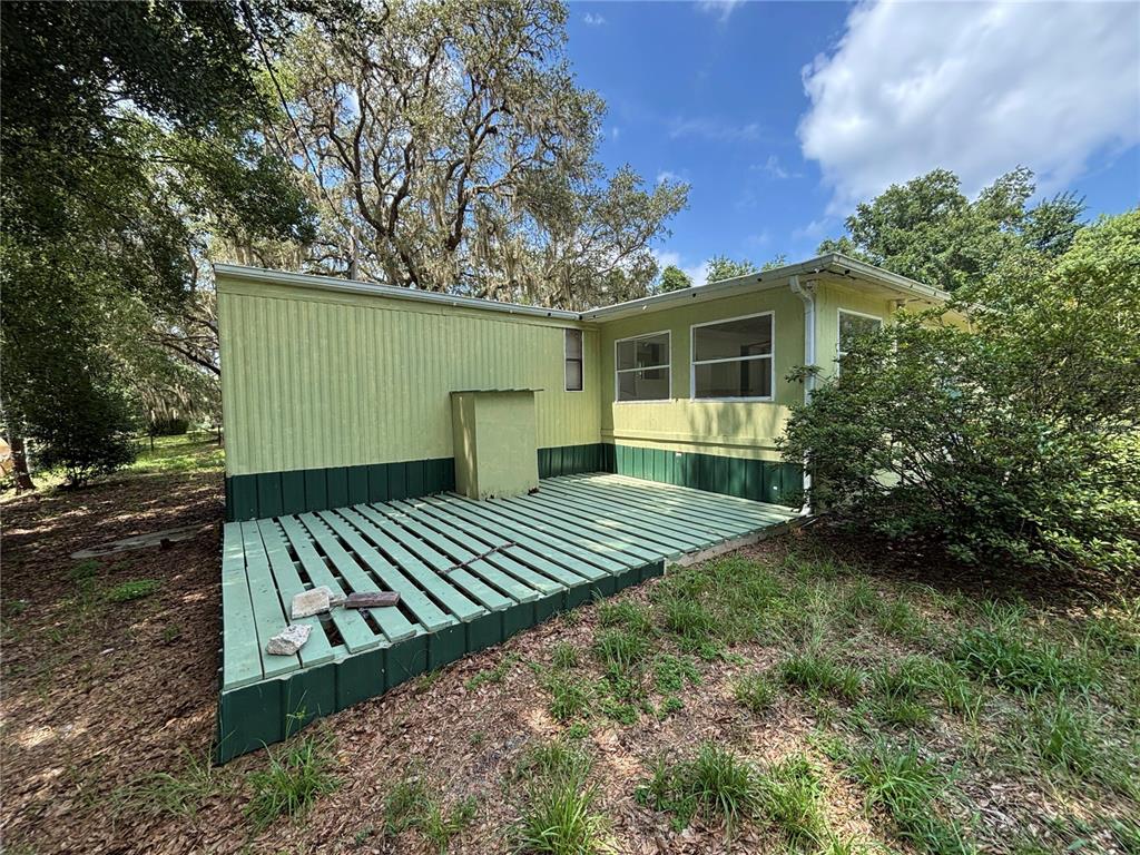 A light green mobile home exterior features a wooden deck and a small utility enclosure — 18274 SE 22ND PLACE, SILVER SPRINGS, FL