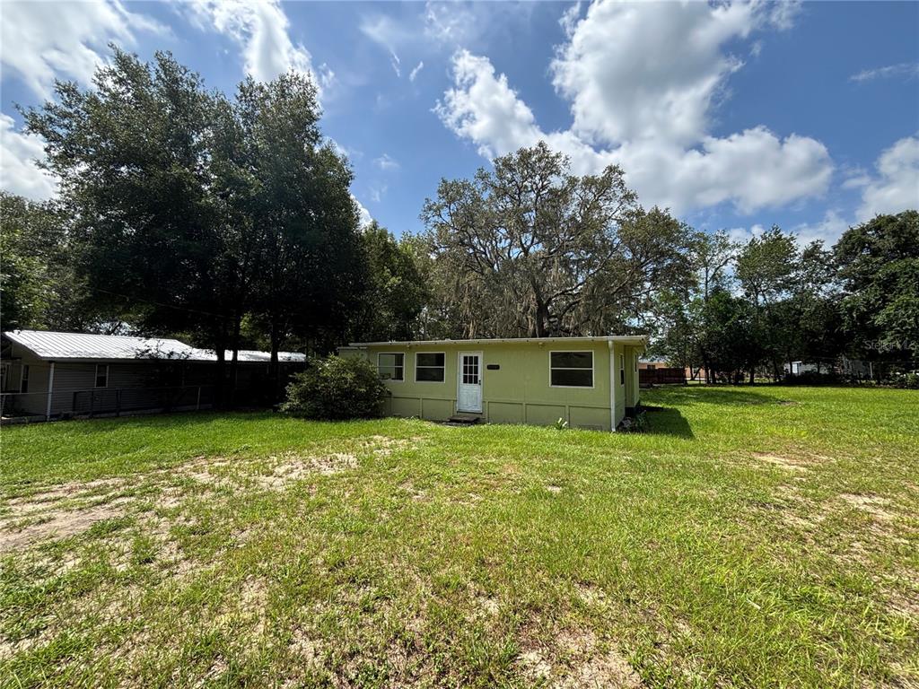 A light green, single-story house sits on a large, grassy lot under a blue sky — 18274 SE 22ND PLACE, SILVER SPRINGS, FL